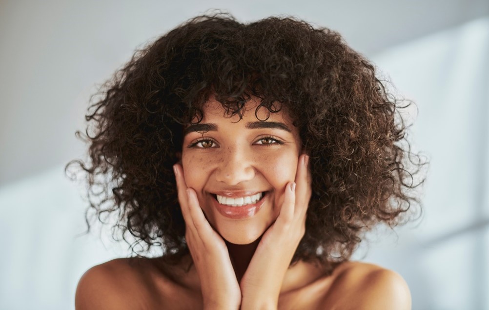 A person with curly hair holding her face