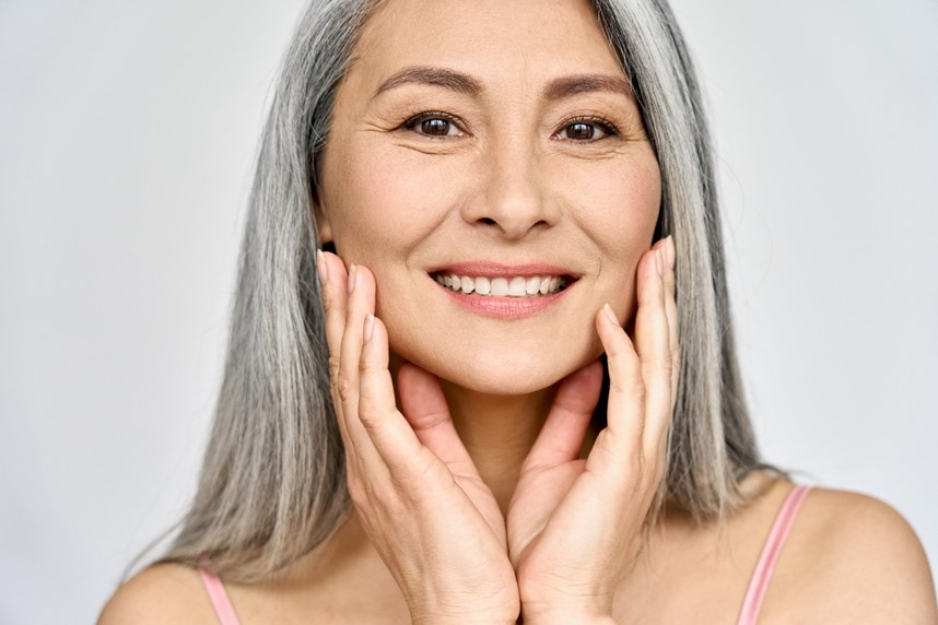 A person with grey hair and pink top touching her face